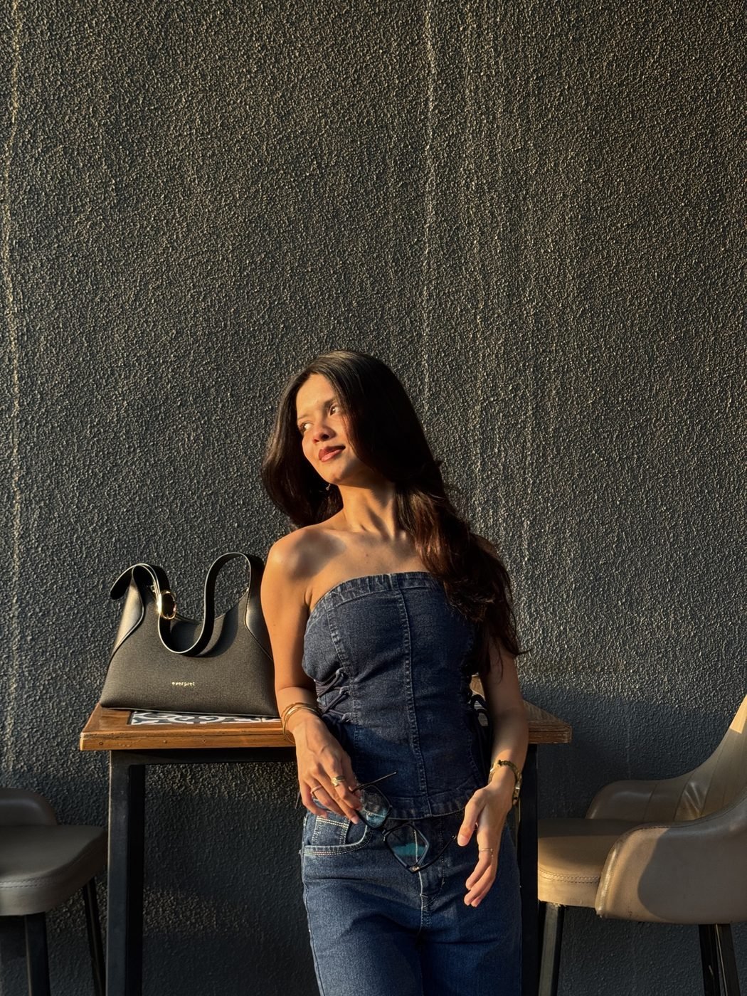 Disha Rokde in a denim corset and jeans against a dark textured wall