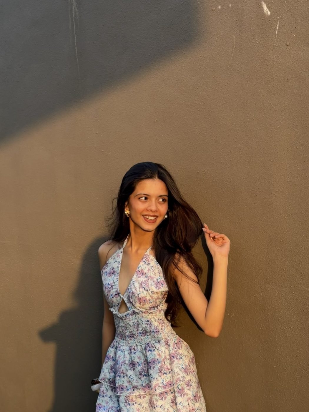 Disha Rokde in a floral summer dress against a sunlit wall